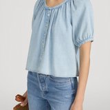 Woman wearing a light blue denim top and jeans against a plain background
