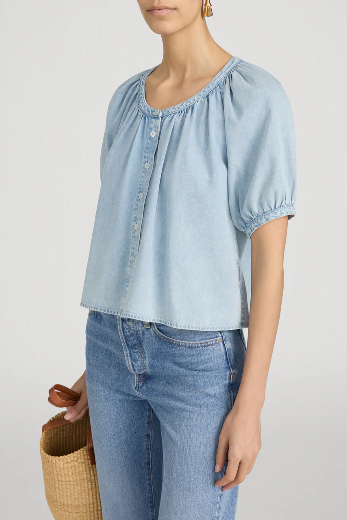 Woman wearing a light blue denim top and jeans against a plain background