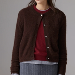 A woman wearing a dark brown fuzzy button-up cardigan over a burgundy sweater and a gray pinstriped skirt, photographed against a neutral gray studio background.
