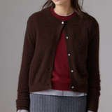 A woman wearing a dark brown fuzzy button-up cardigan over a burgundy sweater and a gray pinstriped skirt, photographed against a neutral gray studio background.