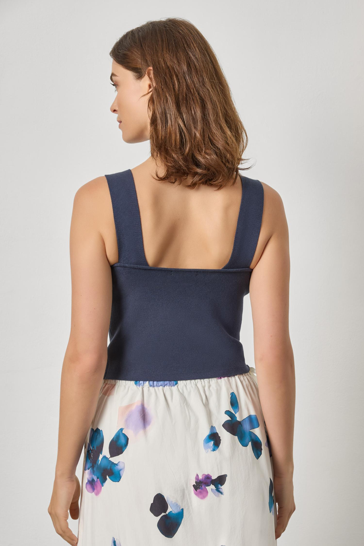 Woman wearing a navy top and floral skirt on a plain background