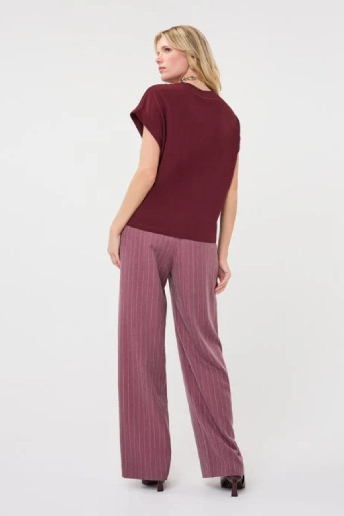 A woman shown from the back wearing a short-sleeve maroon top and mauve wide-leg pinstripe trousers against a plain white studio background.