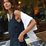 Woman in a dark blue dress with a white shirt over her shoulder, standing on a tiled patio.