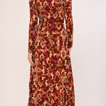 A woman modeling a long-sleeve midi dress with a red, orange, and beige floral ikat pattern, shown from the back against a plain light background.
