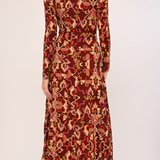 A woman modeling a long-sleeve midi dress with a red, orange, and beige floral ikat pattern, shown from the back against a plain light background.