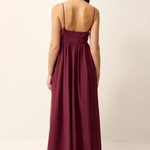 A woman wearing a long, sleeveless maxi dress in a deep burgundy or plum color, shown from the back against a plain off-white studio background.