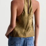 A woman shown from the back wearing a metallic gold halter top and blue jeans against a plain light gray studio background.