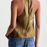 A woman shown from the back wearing a metallic gold halter top and blue jeans against a plain light gray studio background.