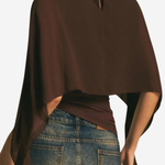 A woman shown from the back wearing a dark brown draped poncho-style top with a small keyhole cutout at the neckline, paired with blue jeans.