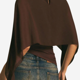 A woman shown from the back wearing a dark brown draped poncho-style top with a small keyhole cutout at the neckline, paired with blue jeans.