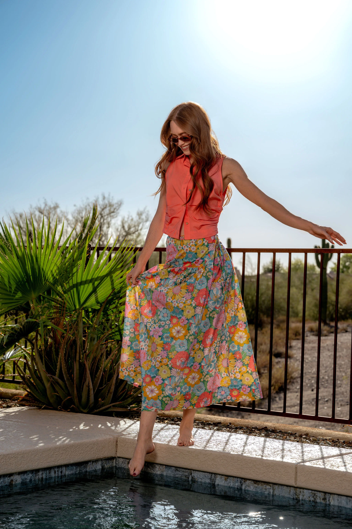 Woman in a colorful dress standing by a pool with a desert landscape in the background