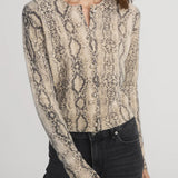 Woman wearing a snake print blouse with long sleeves on a plain background