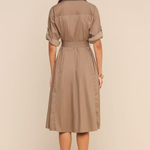 A woman viewed from the back wearing a taupe-brown short-sleeve collared shirt dress with a matching waist tie, paired with beige high-heeled sandals, against a solid beige studio background.