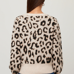 A woman viewed from the back wearing a cream-colored knit sweater with a black leopard print pattern and blue jeans, set against a plain light gray background.