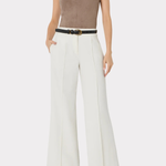 A model wearing a sleeveless taupe-brown V-neck top, white wide-leg trousers with a thin black belt, and black pointed shoes, photographed against a light gray studio background.
