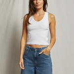 Woman wearing a white tank top and blue jeans against a plain background