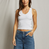 Woman wearing a white tank top and blue jeans against a plain background
