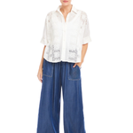 Woman wearing a white blouse with lace details and blue wide-leg jeans on a white background