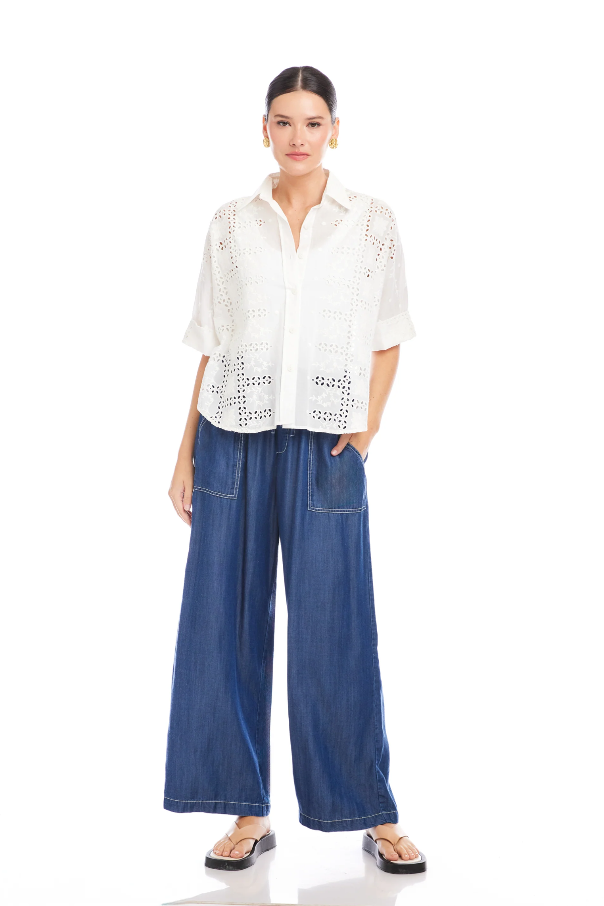 Woman wearing a white blouse with lace details and blue wide-leg jeans on a white background