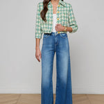 Woman wearing a green patterned jacket and blue jeans on a plain background