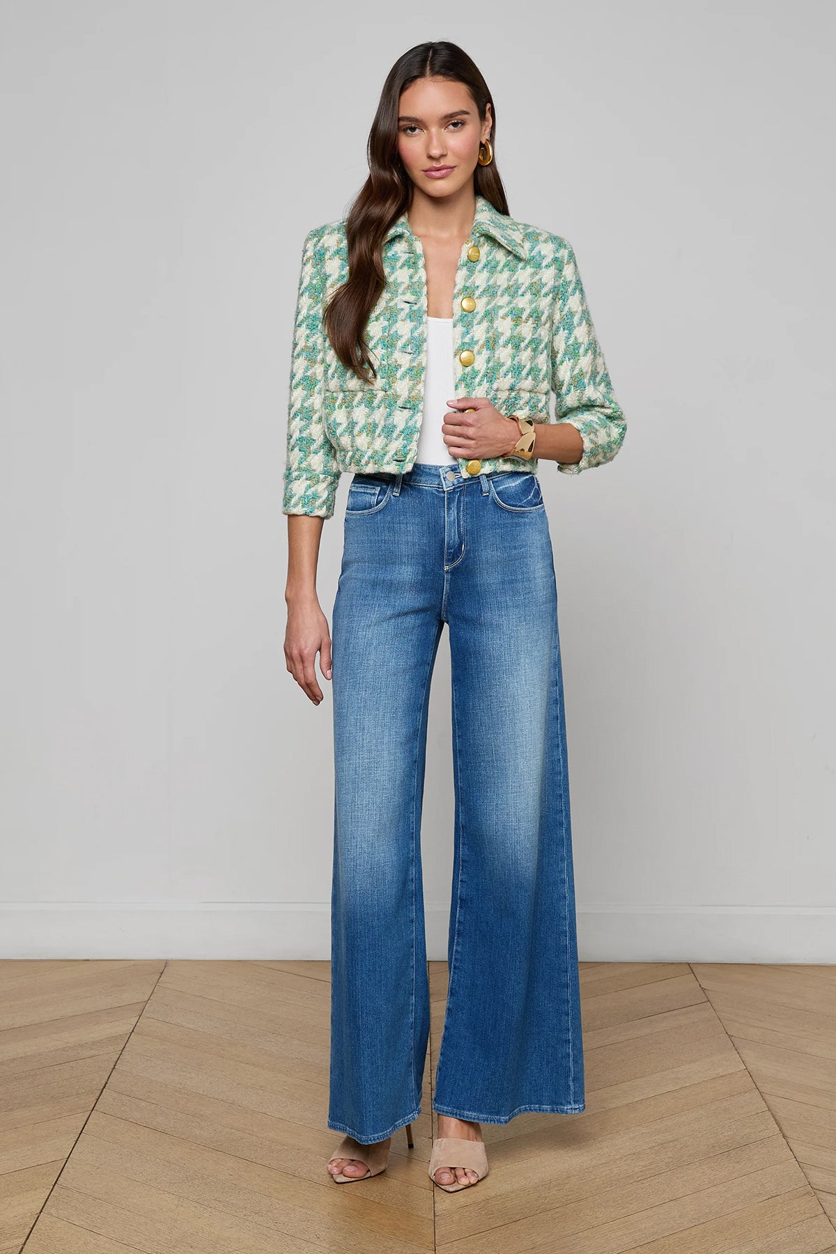 Woman wearing a green patterned jacket and blue jeans on a plain background