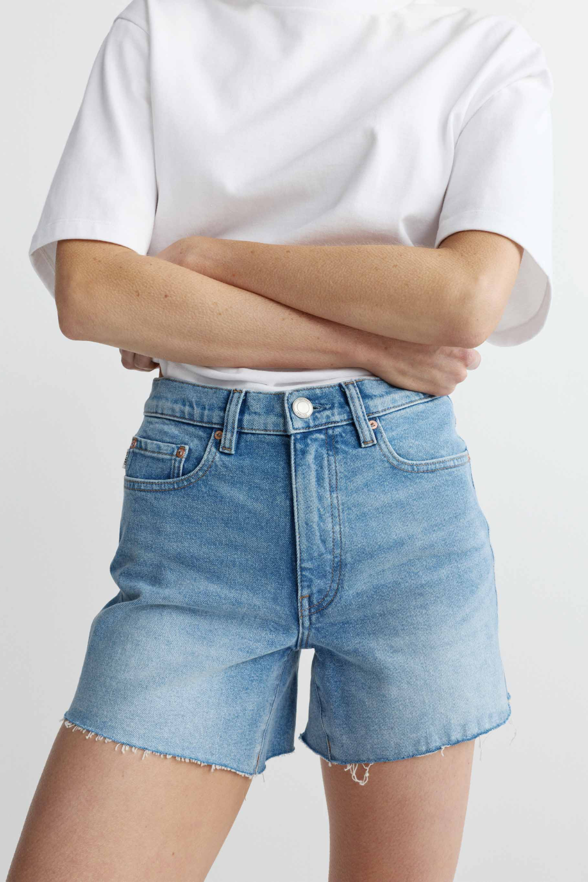 Person wearing light blue denim shorts and a white t-shirt on a plain background