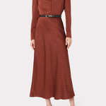 A woman modeling a rust-brown long-sleeve midi dress with a subtle polka dot pattern, a pointed collar, and a black belt with a silver buckle at the waist, set against a plain light gray background.