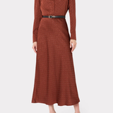 A woman modeling a rust-brown long-sleeve midi dress with a subtle polka dot pattern, a pointed collar, and a black belt with a silver buckle at the waist, set against a plain light gray background.