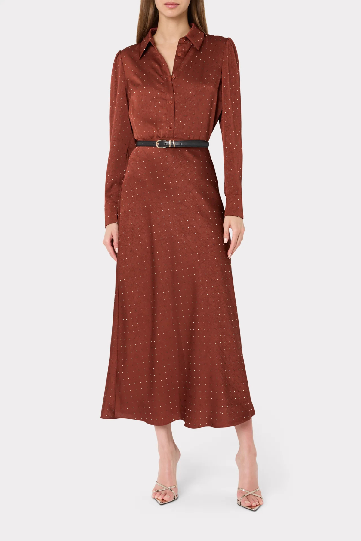 A woman modeling a rust-brown long-sleeve midi dress with a subtle polka dot pattern, a pointed collar, and a black belt with a silver buckle at the waist, set against a plain light gray background.