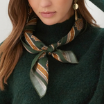 A close-up of a woman wearing a dark green knit sweater and a patterned silk scarf tied around her neck. The scarf features green, gold, and brown geometric and floral motifs.