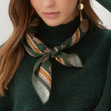 A close-up of a woman wearing a dark green knit sweater and a patterned silk scarf tied around her neck. The scarf features green, gold, and brown geometric and floral motifs.