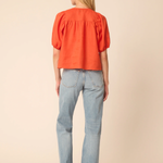 Woman wearing an orange blouse and light blue jeans on a beige background