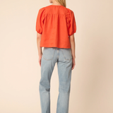 Woman wearing an orange blouse and light blue jeans on a beige background