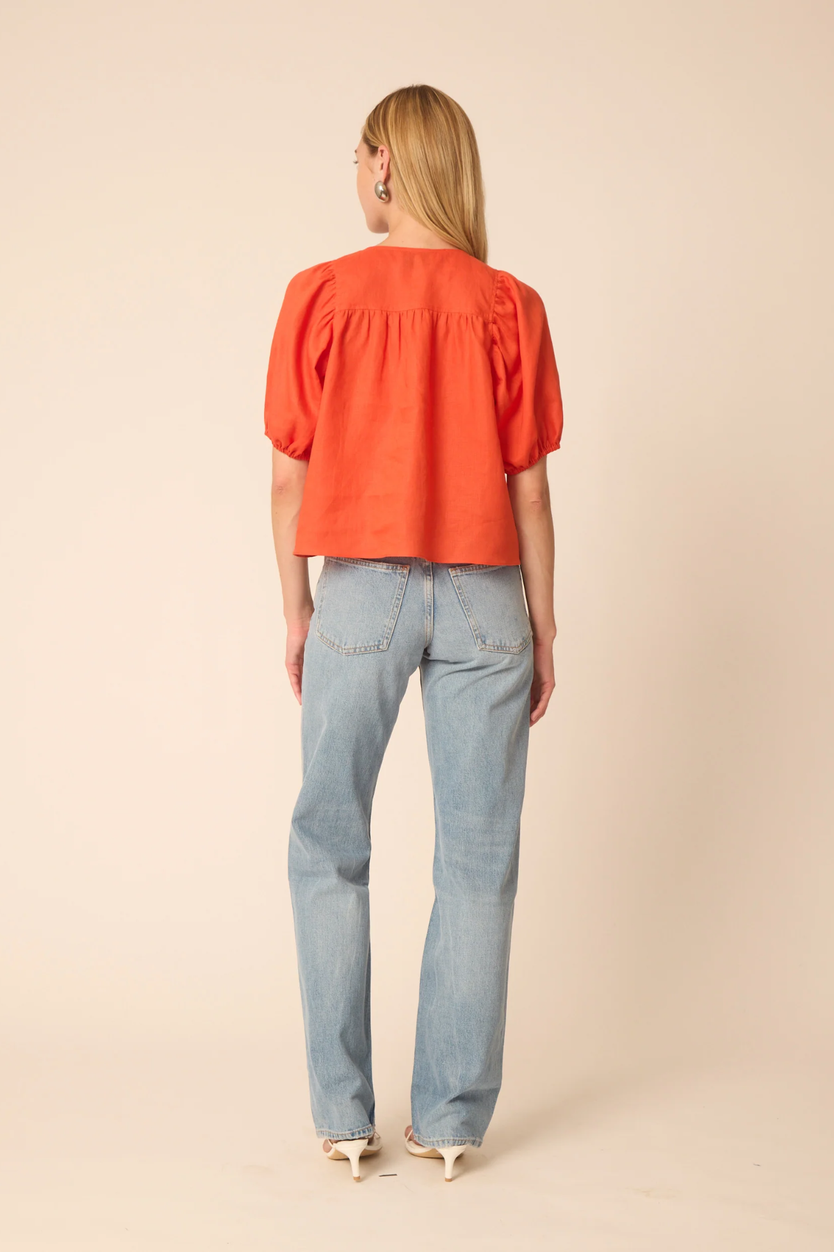 Woman wearing an orange blouse and light blue jeans on a beige background