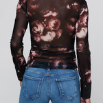A model shown from the back wearing a sheer long-sleeve collared top with a dark brown and dusty rose floral print, paired with blue jeans, against a light gray background.