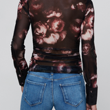 A model shown from the back wearing a sheer long-sleeve collared top with a dark brown and dusty rose floral print, paired with blue jeans, against a light gray background.