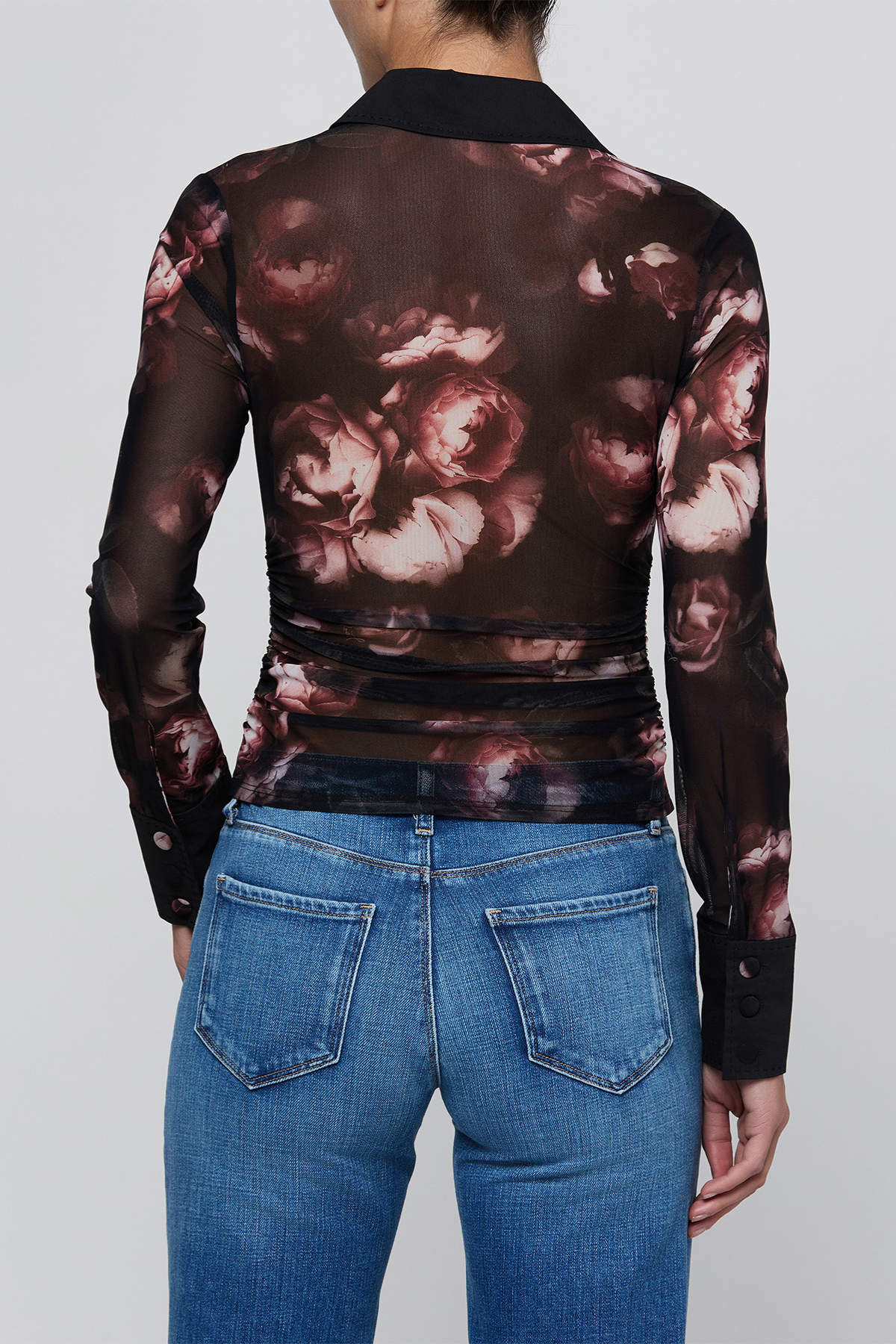 A model shown from the back wearing a sheer long-sleeve collared top with a dark brown and dusty rose floral print, paired with blue jeans, against a light gray background.