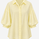 A pale yellow button-up blouse with a pointed collar, 3/4 puff sleeves, and a relaxed silhouette, shown against a plain white background.