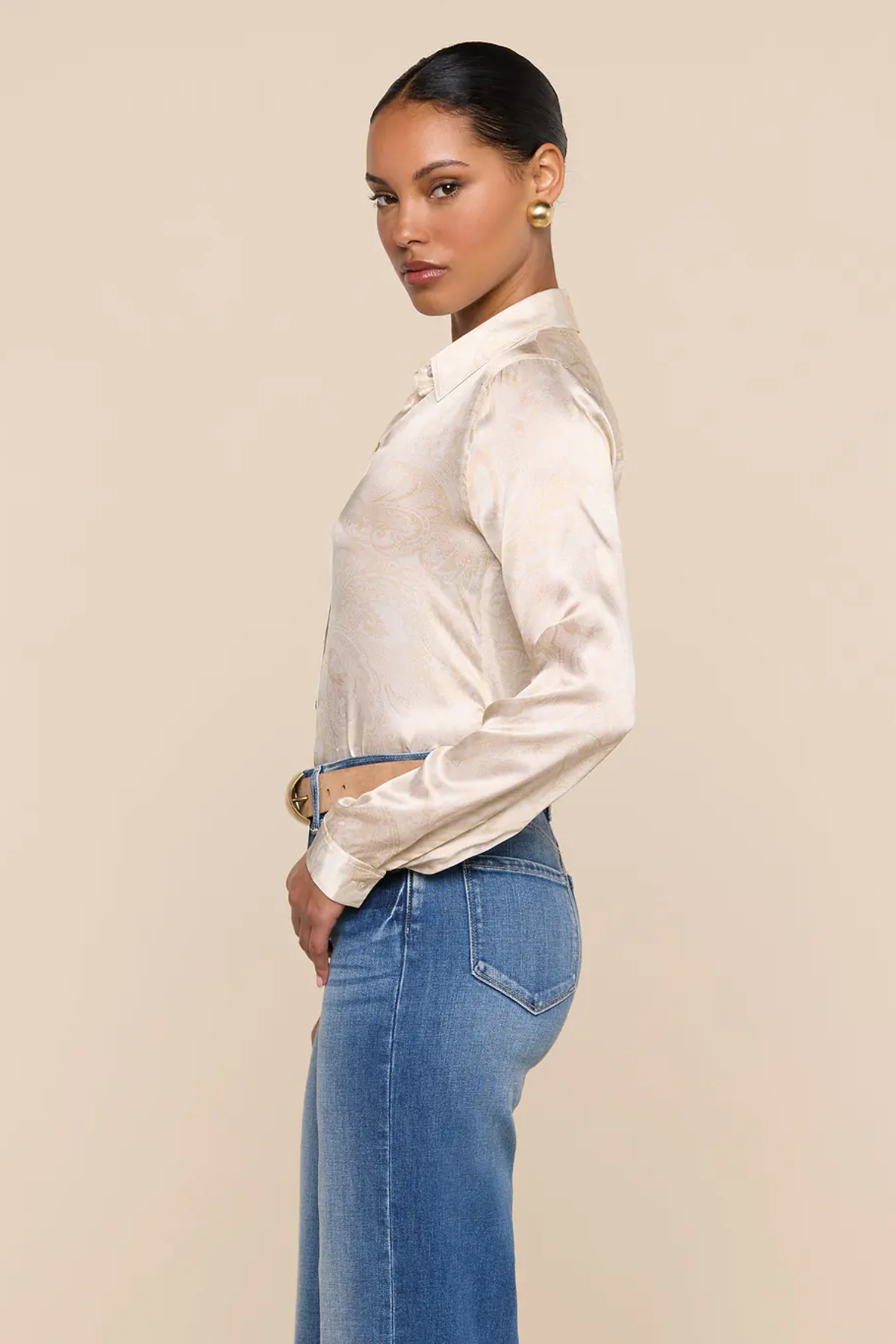 Woman wearing a white blouse and blue jeans against a beige background