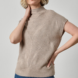 A woman wearing a beige ribbed knit mock-neck sweater vest with short sleeves, paired with blue jeans, against a light gray studio background.
