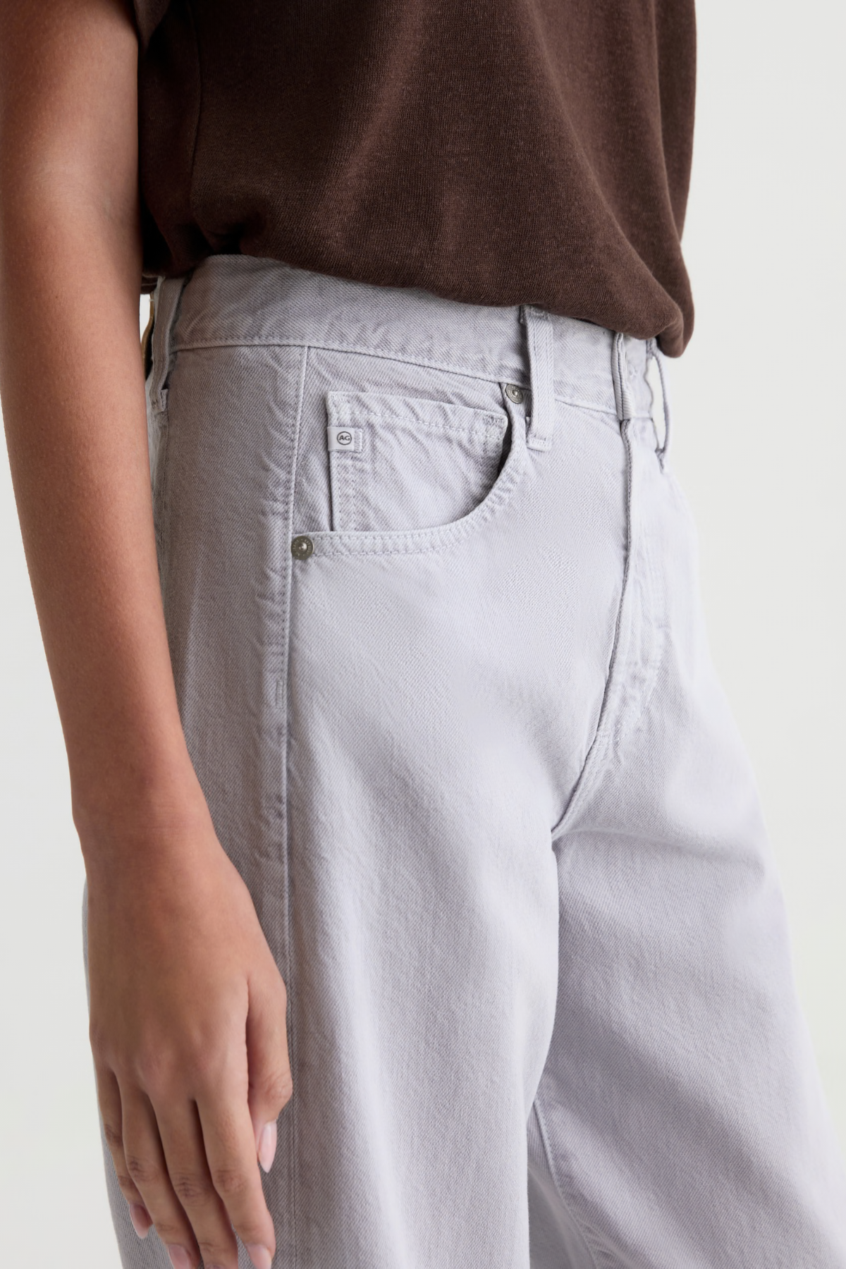 Close-up of a person wearing light gray wide-leg jeans with a brown top, showing the back pocket and waistband area against a plain light background.