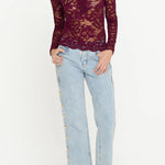 Woman wearing a burgundy lace top and light blue jeans on a white background