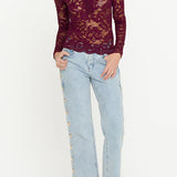 Woman wearing a burgundy lace top and light blue jeans on a white background