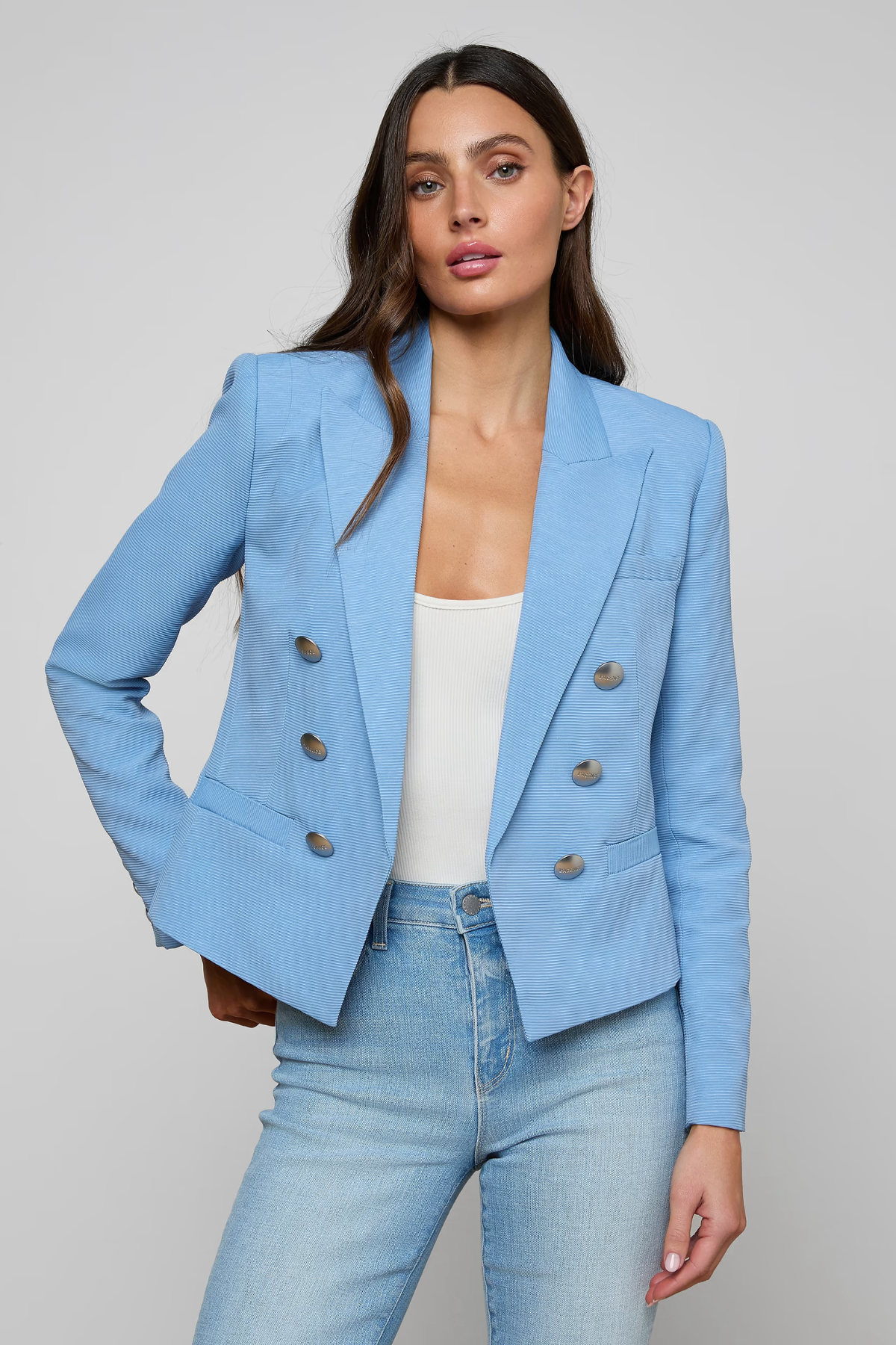 Woman wearing a light blue blazer and jeans on a gray background