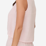 A woman shown from the side wearing a sleeveless light pink top and matching light pink bottoms against a plain light background.