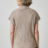 A woman shown from the back wearing a beige short-sleeve ribbed knit mock neck sweater and blue jeans against a light gray studio background.