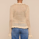 Person wearing a beige crochet top and blue jeans on a beige background