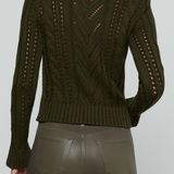 An olive green cable-knit cropped sweater with openwork details on the back, shown on a model from behind against a light gray background.