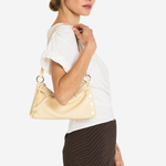 A woman in a white short-sleeve top and dark brown pinstriped skirt carries a light beige leather shoulder bag with gold-tone hardware against a plain white background.