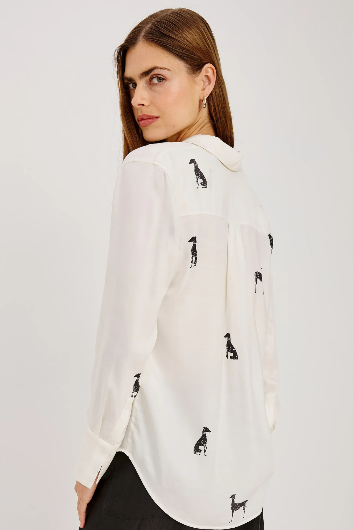 A woman wearing a white long-sleeve blouse with black dog silhouettes printed all over it, shown from a side-back angle against a plain light gray studio background.